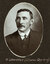 Black and white oval photograph of a man in a suit with his name written underneath on the mount