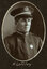 Black and white oval photograph of a man in a uniform and cap with his name written underneath on the mount