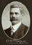 Black and white oval photograph of a man in a suit with his name written underneath on the mount