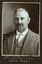 Black and white photograph of a man in a suit with his name written underneath on the mount