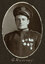 Black and white oval photograph of a man in a uniform and cap with his name written underneath on the mount