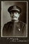 Black and white photograph of a man in a uniform and cap with his name written underneath on the mount