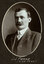 Black and white oval photograph of a man in a suit with his name written underneath on the mount