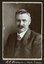 Black and white photograph of a man in a suit with his name written underneath on the mount