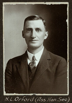 Black and white photograph of a man in a suit with his name written underneath on the mount