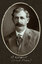 Black and white oval photograph of a man in a suit with his name written underneath on the mount