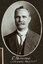 Black and white oval photograph of a man in a suit with his name written underneath on the mount