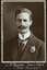Black and white photograph of a man in a suit with his name written underneath on the mount