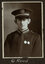 Black and white photograph of a man in a uniform and cap with his name written underneath on the mount