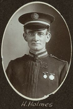 Black and white oval photograph of a man in a uniform and cap with his name written underneath on the mount