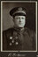 Black and white photograph of a man in a uniform and cap with his name written underneath on the mount