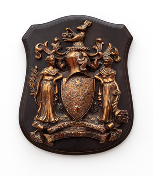 Metal Victorian coat of arms in relief on a wooden plaque. There are two female figures standing on a mound of grass flanking the Southern Cross Shield, above it is a knight's helmet and a Kangaroo holding a crown.