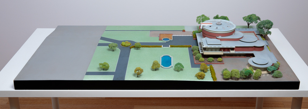 Architectural model of a cylindrical building in orange brick surrounded by gardens and paths
