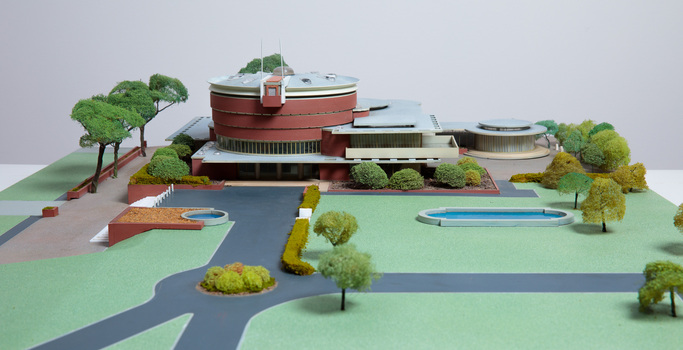 Architectural model of a cylindrical building in orange brick surrounded by gardens and paths