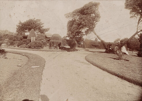 Sepia toned photograph of a formal garden with winding paths and vegetation, the photograph has large scratches
