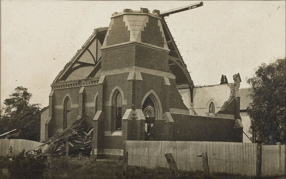 Sepia photograph of a church damaged by a cyclone, without a roof, windows and wall missing, fence fallen over