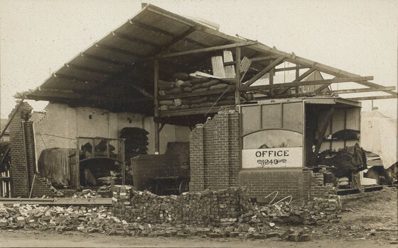Sepia photograph of a factory building damaged by a cyclone, missing walls and a roof, building debris all around it
