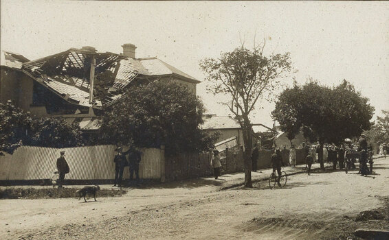Sepia photograph of a subruban street with houses damaged by cyclone, people looking at the damage