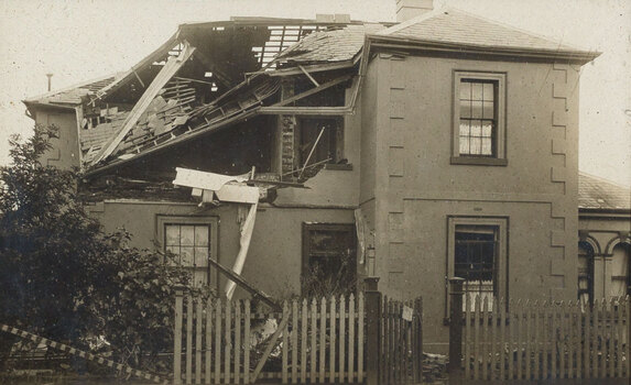 Sepia photograph of a concrete house damaged by a cyclone - the roof is partially off and is missing a wall on the second story