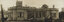 Sepia photograph of a grand house with a tower that has been damaged by cyclone - the roof of the front verandah has collapsed, and trees are broken in the garden