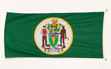 Green flag with central coat of arms depicting a market gardener and an aboriginal figure flanking a shield, a cornucopia and a seagull. The motto FRUCTU NOSCITUR is in a banner below.
