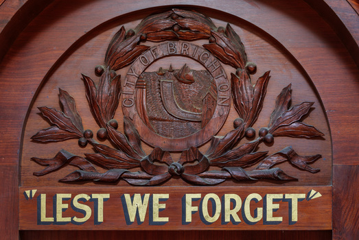 Detail of an honour board sowing a carved wreath containing City of Brighton Crest and below that gold and black lettering "LEST WE FORGET"