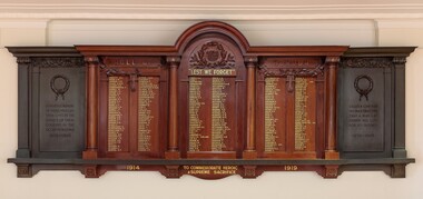 Large rectangular shaped timber and metal honour board attached to a white wall. Names honouring fallen soldiers written in gold lettering. 