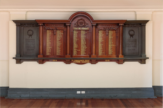 Large rectangular shaped timber and metal honour board attached to a white wall. Names honouring fallen soldiers written in gold lettering. 