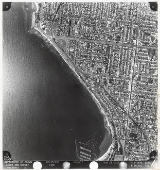 Black and white aerial photograph of a coastal suburban area with the bay to the left and land on the right. Text in the bottom margin