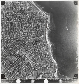 Black and white aerial photograph with a coastal suburb on the left and bay on the right. The photograph has a white border with text in a black margin at the bottom.
