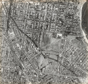 Black and white aerial photograph of a coastal suburb featuring a large park lower centre