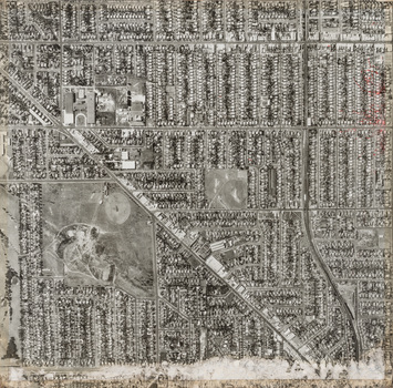 Black and white aerial photograph of streets lined with buildings, a large park is situated lower left.