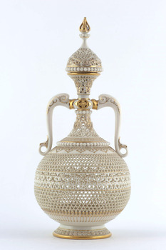 White ceramic vase and lid with cork stopper. Holes in body and curved handles. Gold painted decoration over most of body clearly seen on top and bottom rims.
