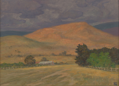 Open paddocks landscape with treed fence line leading to building in mid ground. There is a stand of trees opposite building. Large bare hill in background with expressive grey clouds in sky.