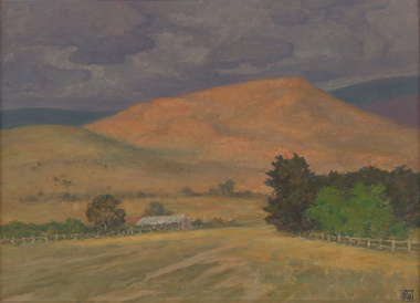Open paddocks landscape with treed fence line leading to building in mid ground. There is a stand of trees opposite building. Large bare hill in background with expressive grey clouds in sky.