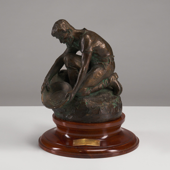 A man kneels holding a pan as if panning for gold