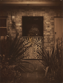 A view of a white half gate attached to a brik wall with an exterior light to the upper left.