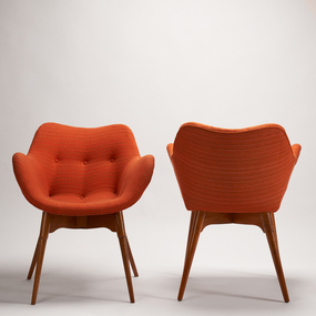 Two chairs in a tub shape covered in orange fabric with 6 buttons and wooden legs.