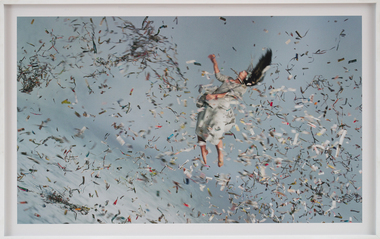 A woman appears mid-air in a white dress with many pieces of tickertape paper floating through the sky with her.