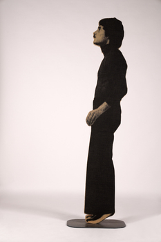A figure made of plywood stands on his tiptoes with his hand slightly extended out to the side.