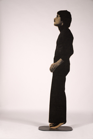 A figure made of plywood stands on his tiptoes with his hand slightly extended out to the side.
