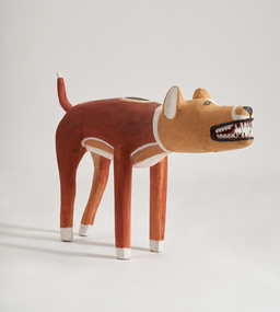 A dog stands on four legs with its jaw slightly apart revealing teeth. Its body is a dark orange colour and its head is in a golden colour.