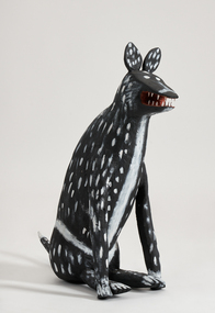 A black and white spotted dog sits upright with its jaw slightly apart revealing teeth.