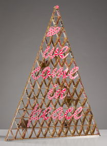 A triangular tower of playing cards adhered together with cut out letters reading "We Come in Peace" adhered to the front frame work.