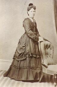 COPY OF A PHOTOGRAPH OF LADY; MARY ANN BROWN (NEE STOWE) STANDING BY BUTTONED ARMCHAIR.