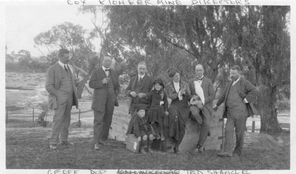 FIve men in suits, one lady, two children sitting on a large crate. One man is holding a cockatoo.