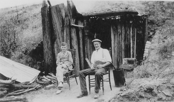 A young man and an older man sitting outside a small building. 