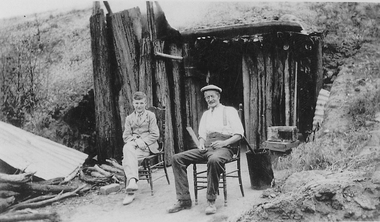 A young man and an older man sitting outside a small building. 