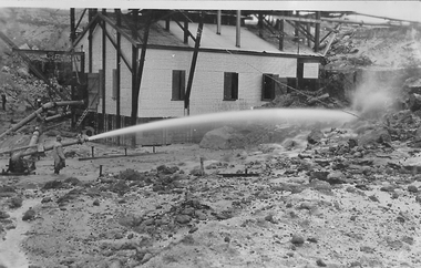 Building with man using sluicing hose in front of it.