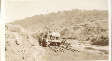Men moving mining equipment along track in dry river bed